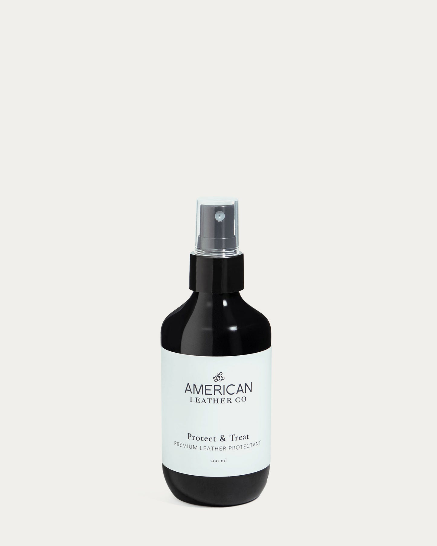A dark spray bottle with the brand "American Leather Co." displays the product name "Protect & Treat Premium Leather Protectant Spray" against a white background. Featuring a pump spray top, this leather treatment offers water repellency and stain resistance for superior care.