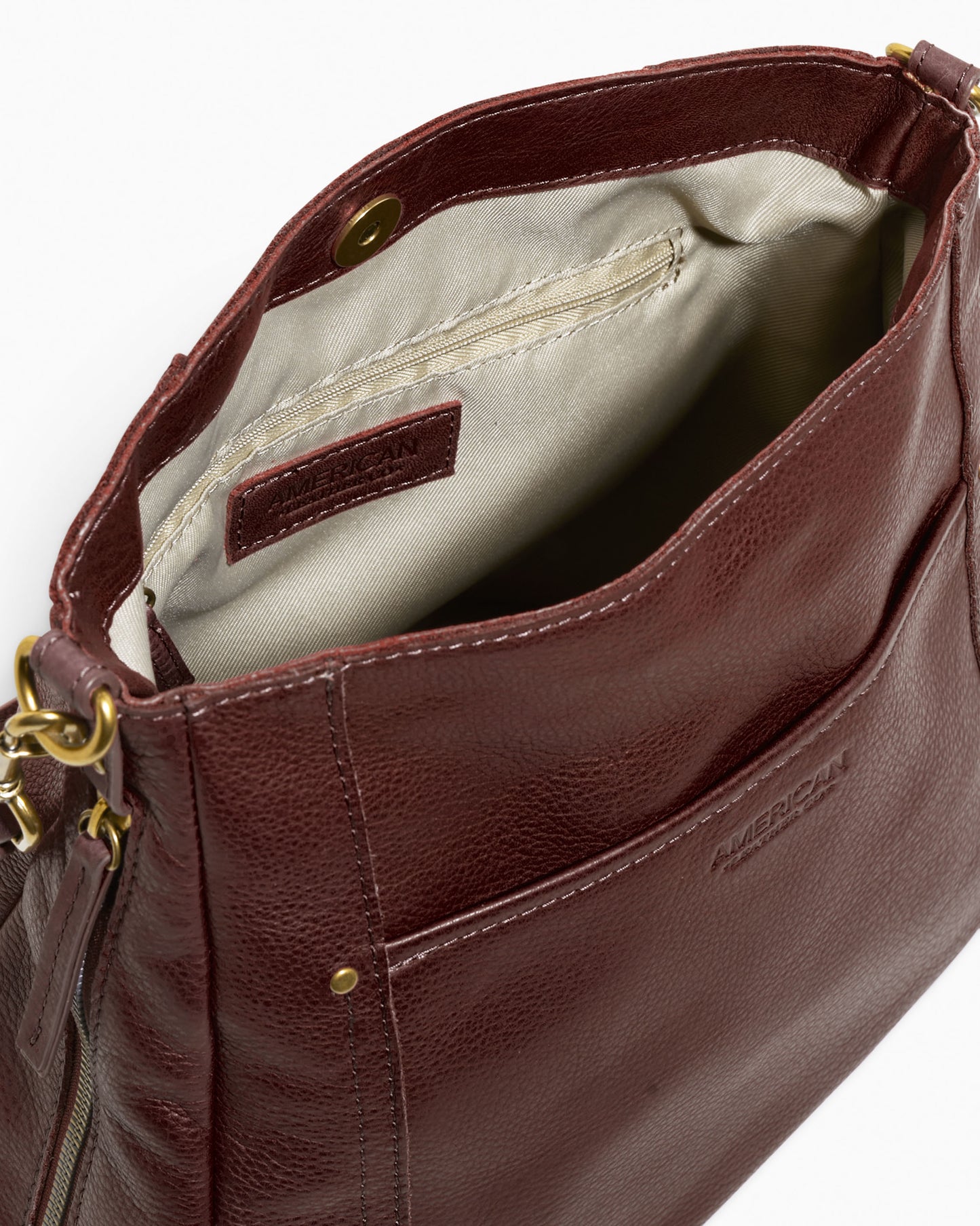 The Austin Convertible Shoulder Crossbody from American Leather Co. is a stylish brown leather bag featuring a visible inner fabric lining and a secure snap closure. It includes a front pocket and brass hardware, with zippers and clasps for the adjustable strap, allowing it to easily convert into a crossbody bag. The brand name is embossed on the exterior.