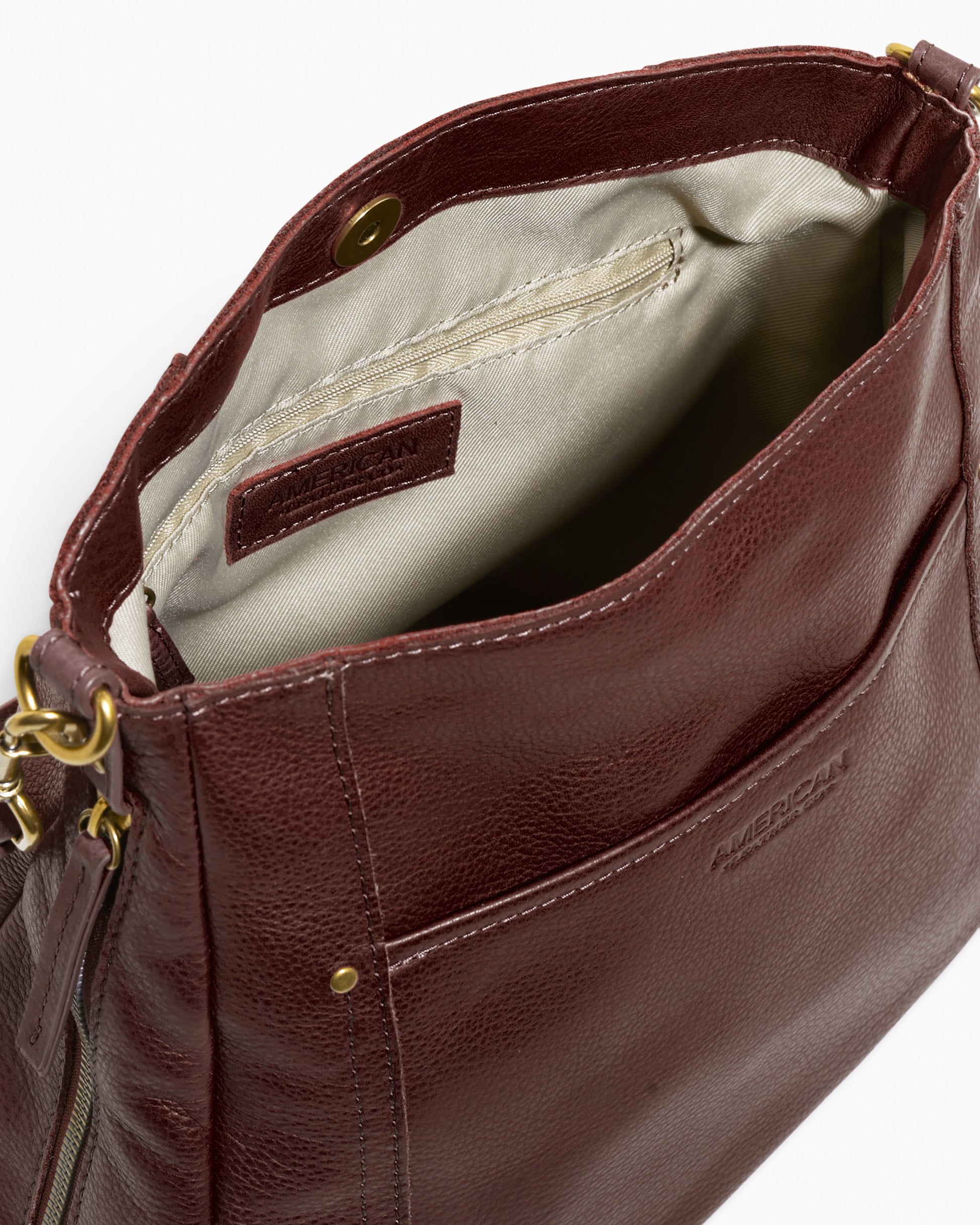 The Austin Convertible Shoulder Crossbody from American Leather Co. is a stylish brown leather bag featuring a visible inner fabric lining and a secure snap closure. It includes a front pocket and brass hardware, with zippers and clasps for the adjustable strap, allowing it to easily convert into a crossbody bag. The brand name is embossed on the exterior.