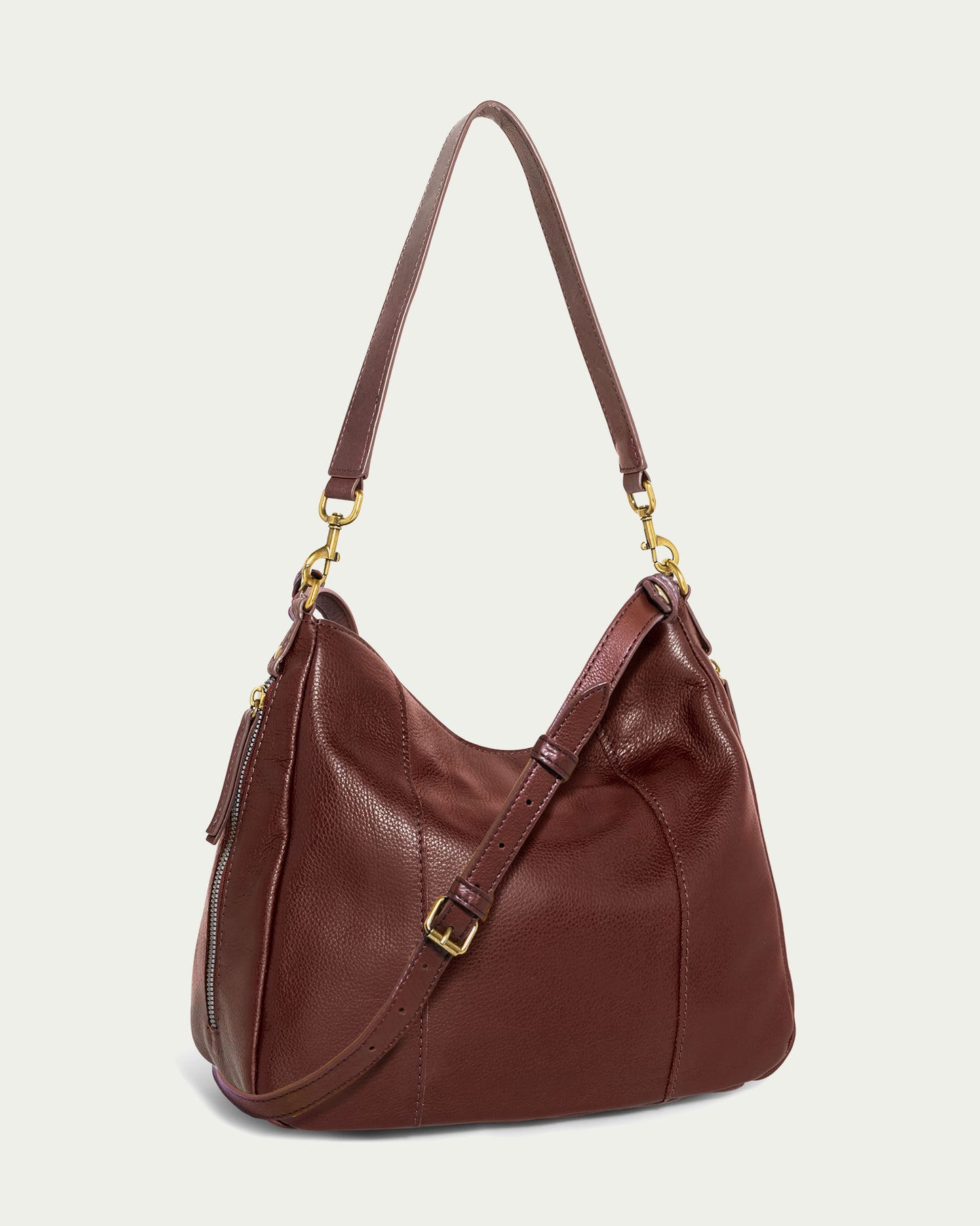 The Austin Convertible Shoulder Crossbody from American Leather Co. is a brown leather bag boasting gold-tone hardware and side zipper pockets. It features a smooth finish, an adjustable strap, and a zippered top, elegantly displayed on a light background.